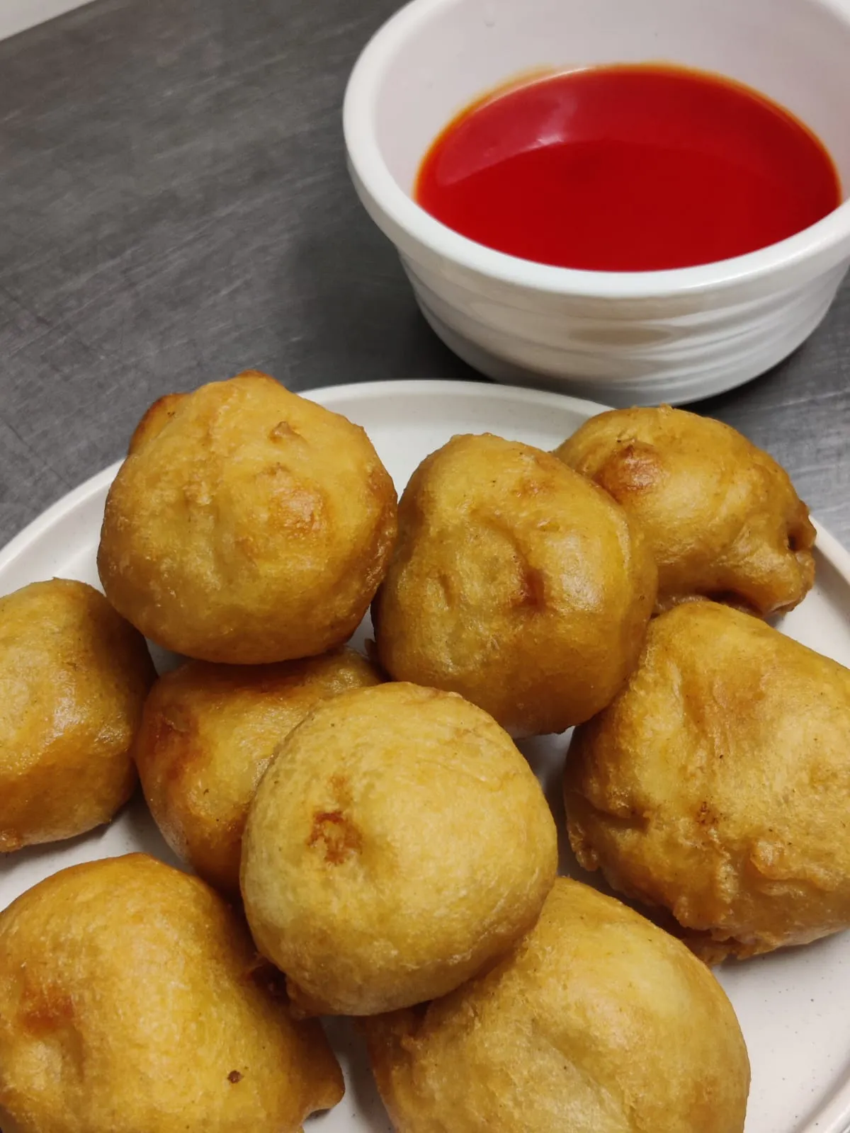 Golden battered fritters piled on a plate with a pot of red dipping sauce