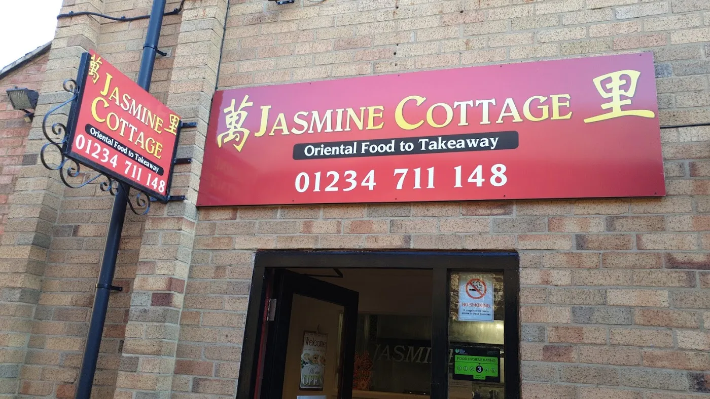 The Jasmine Cottage shopfront: a cerise sign with the name in light capitals, 萬 and 里 at each end, 'Oriental Food to Takeaway' and the phone number, above the shop door